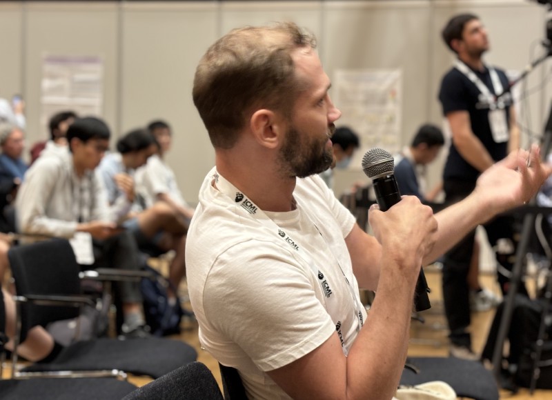 A workshop participants in a white t-shirt holding a microphone asks a question