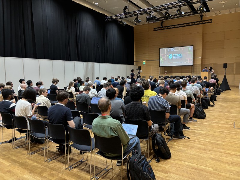 A packed crowd in a conference hall, facing a screen with an ICML logo on it