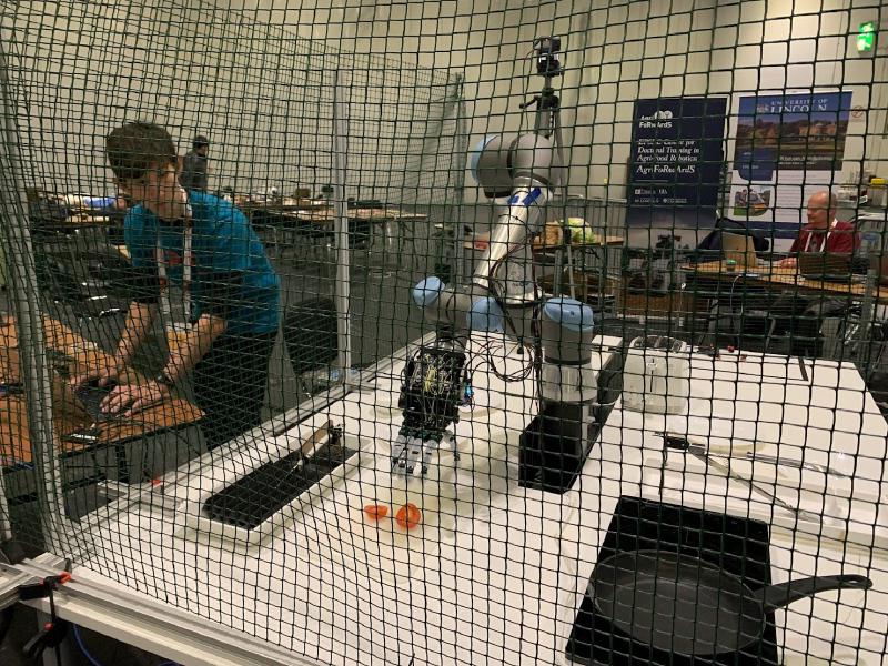 A PhD student controlling a robot hand from his laptop, as it's about to pick up a tomato.