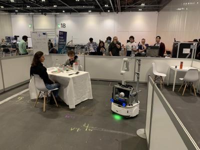 Two people sitting down at a table, with a robot driving up to them