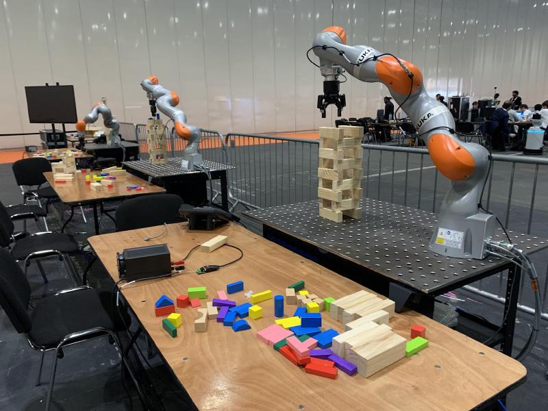Three robot arms stacking jenga blocks